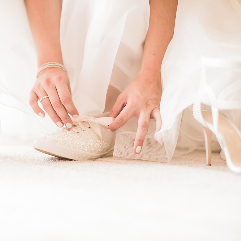 bride getting ready, detail photos, putting on wedding shoes, sneakers with wedding gown, white keds, cielo at castle pines bridal suite, colorado wedding planner