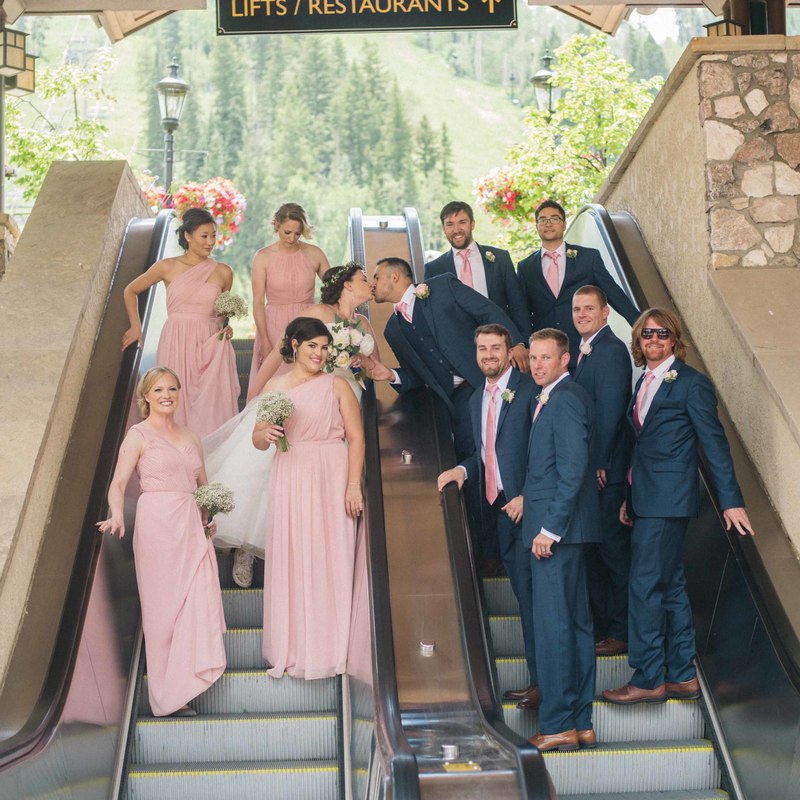 wedding mountain inspiration, beaver creek wedding planner, vail wedding planning, sweetly paired weddings, long pink bridesmaid dresses, blue goomsmen tuxes with pink ties, bride and groom kissing, wedding party portrait on stairs