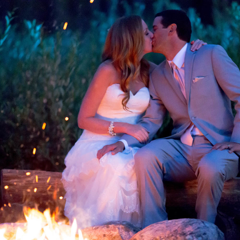 bride and groom sitting next to fire pit at night roasting smores, glamping wedding, piney river ranch wedding planner, mountain wedding inspiration, vail wedding planner, sweetly paired weddings