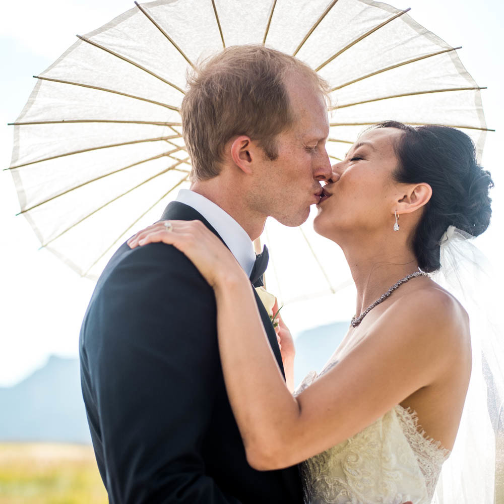 Bride and groom kissing under parasol, boulder wedding planner, colorado wedding planner, classy formal real weddings, sweetly paired