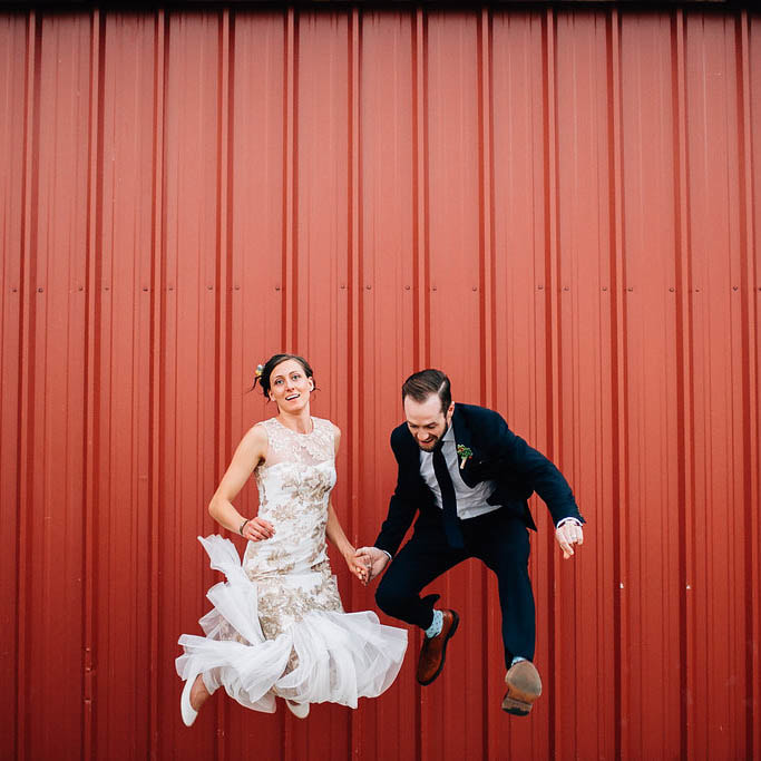 Bride and groom jumping in front of orange wall, denver wedding planner, colorado wedding planner, real weddings, sweetly paired