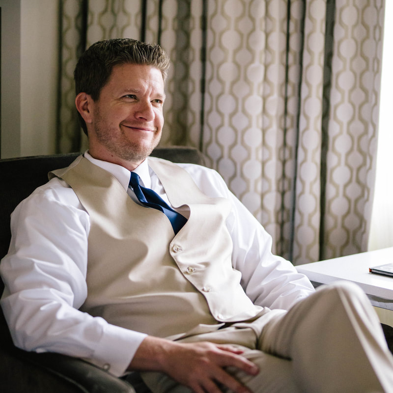 groom getting ready photo, sitting in chair in hotel room, denver wedding planner, colorado wedding planner, khaki suit and vest with navy tie, spruce mountain ranch