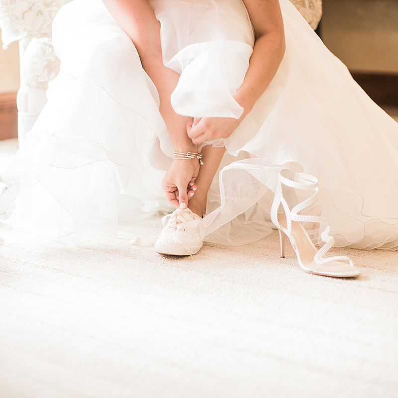bride getting ready, detail photos, putting on wedding shoes, sneakers with wedding gown, white keds, cielo at castle pines bridal suite, colorado wedding planner